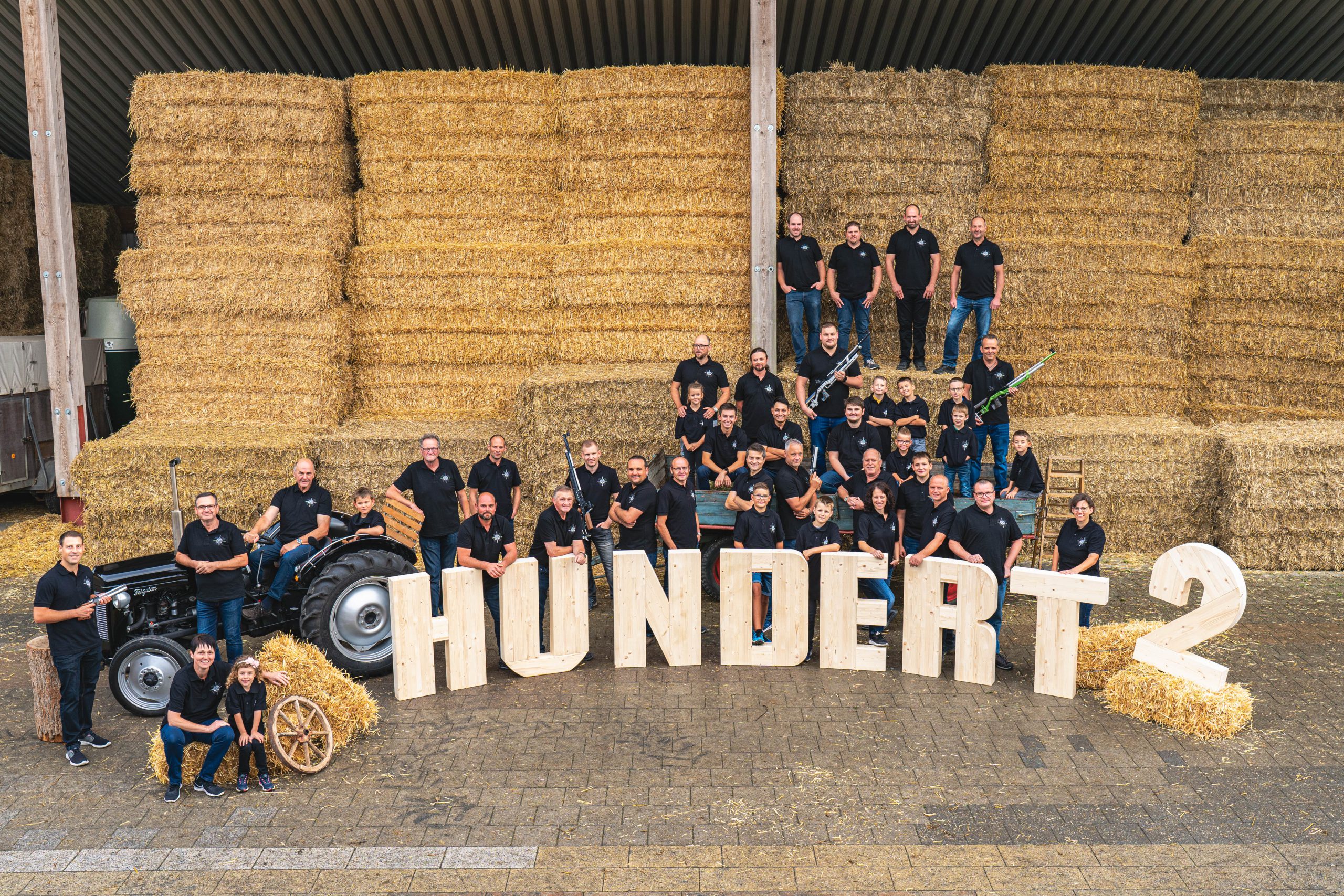 EIne Gruppen Menschen steht für ein Gruppenbild auf Stroballen verteilt um große Buchstaben aus Holz.