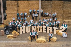 Eine große Gruppe an Menschen mit Musikinstrumenten steht auf Strohballen verteilt.