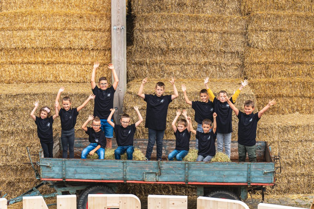 EIne Gruppe Kinder steht auf einem Traktoranhänger und winkt